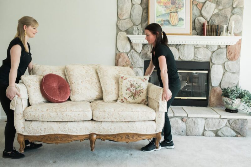 Two Poof team members moving a vintage white couch through a living room