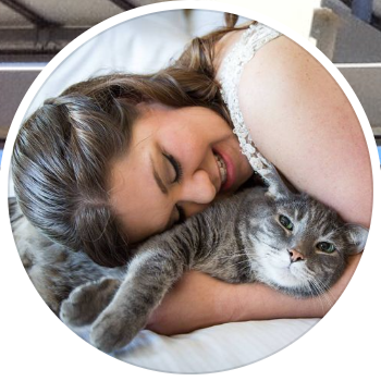 young woman snuggling with her gray cat on a bed