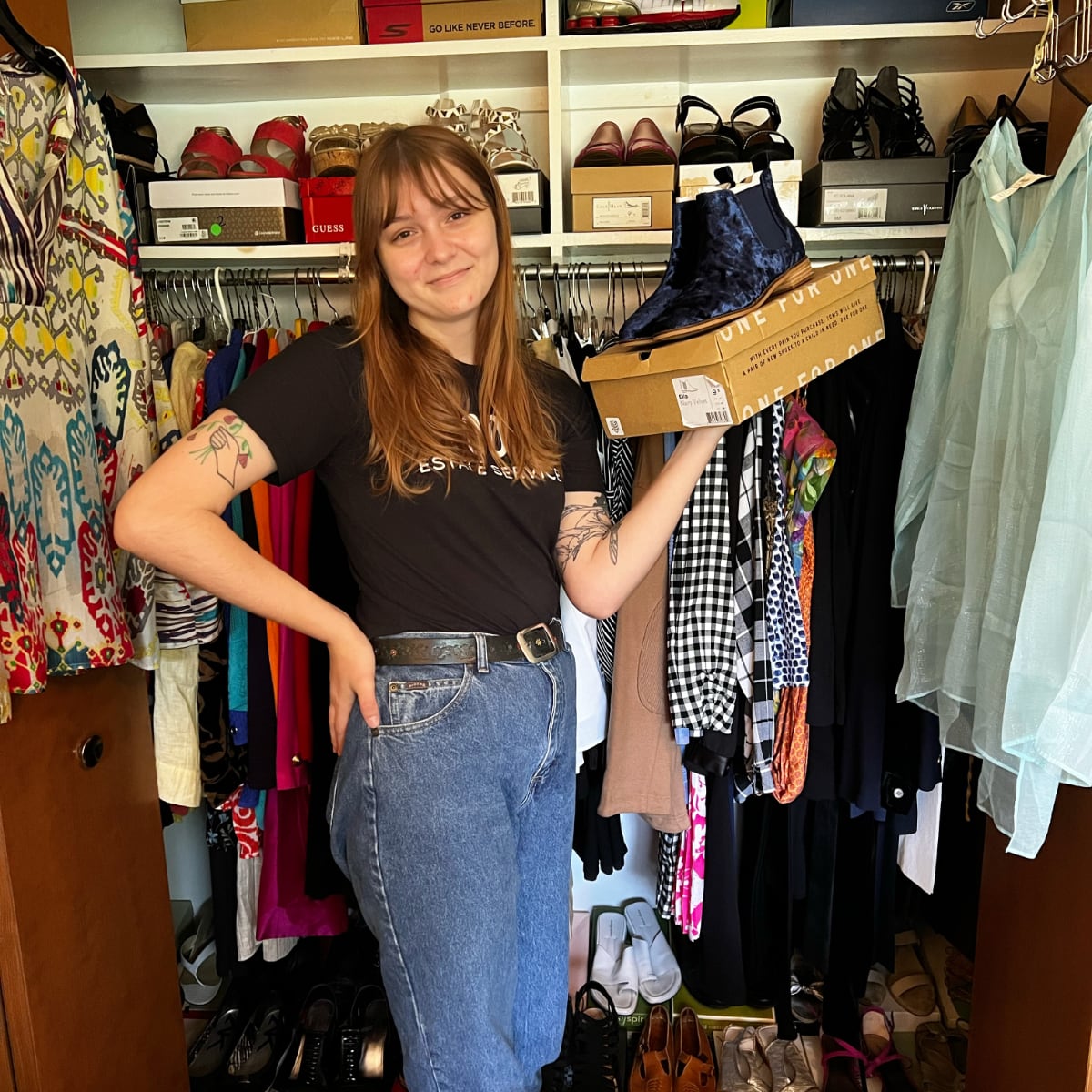 A young woman smiling wearing black tee shirt and jeans holding a shoe box