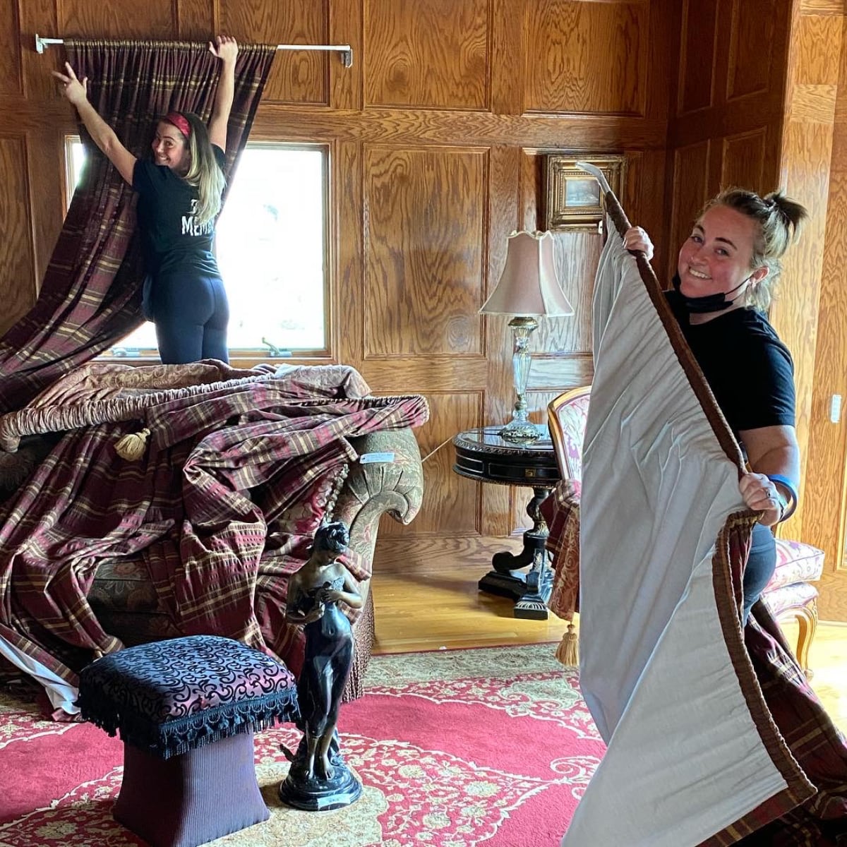 Two young women are taking down curtains while smiling