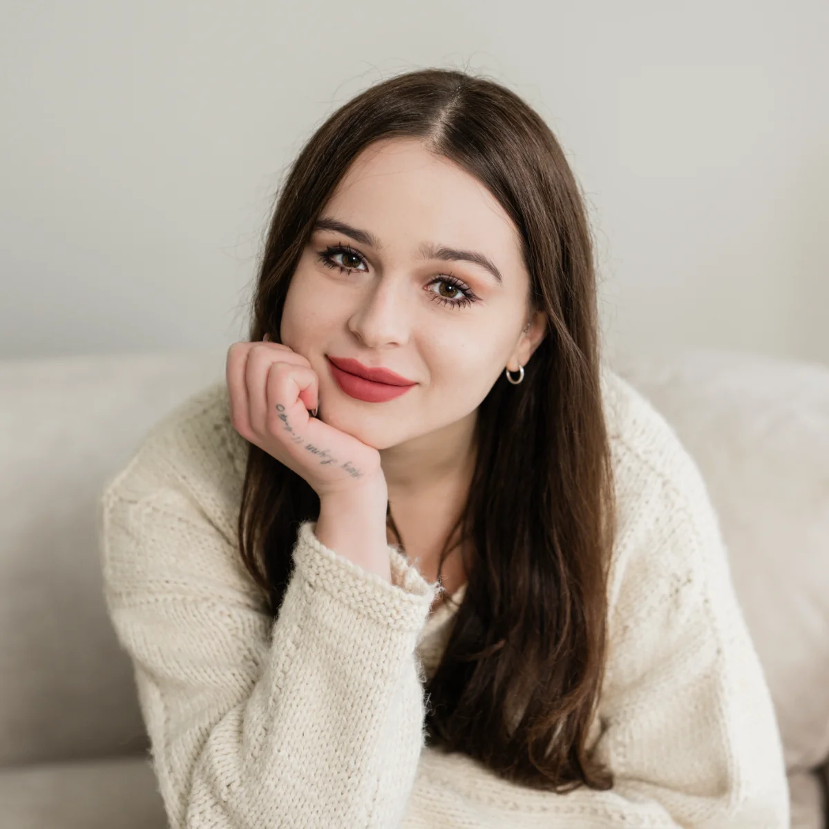 A professional headshot of Maryssa Brown wearing a cream knit sweater. She smiles warmly at the camera while resting her chin on her hand.
