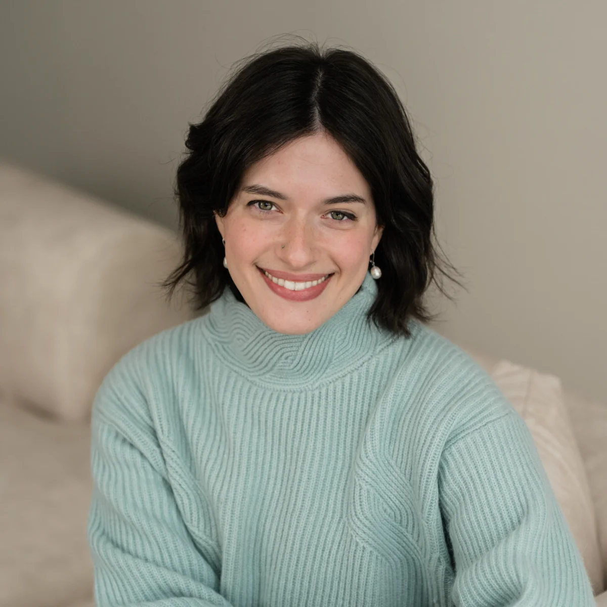 A professional headshot of Shannon Walsh, smiling warmly. She has dark hair and is wearing a light blue ribbed turtleneck sweater and pearl drop earrings.